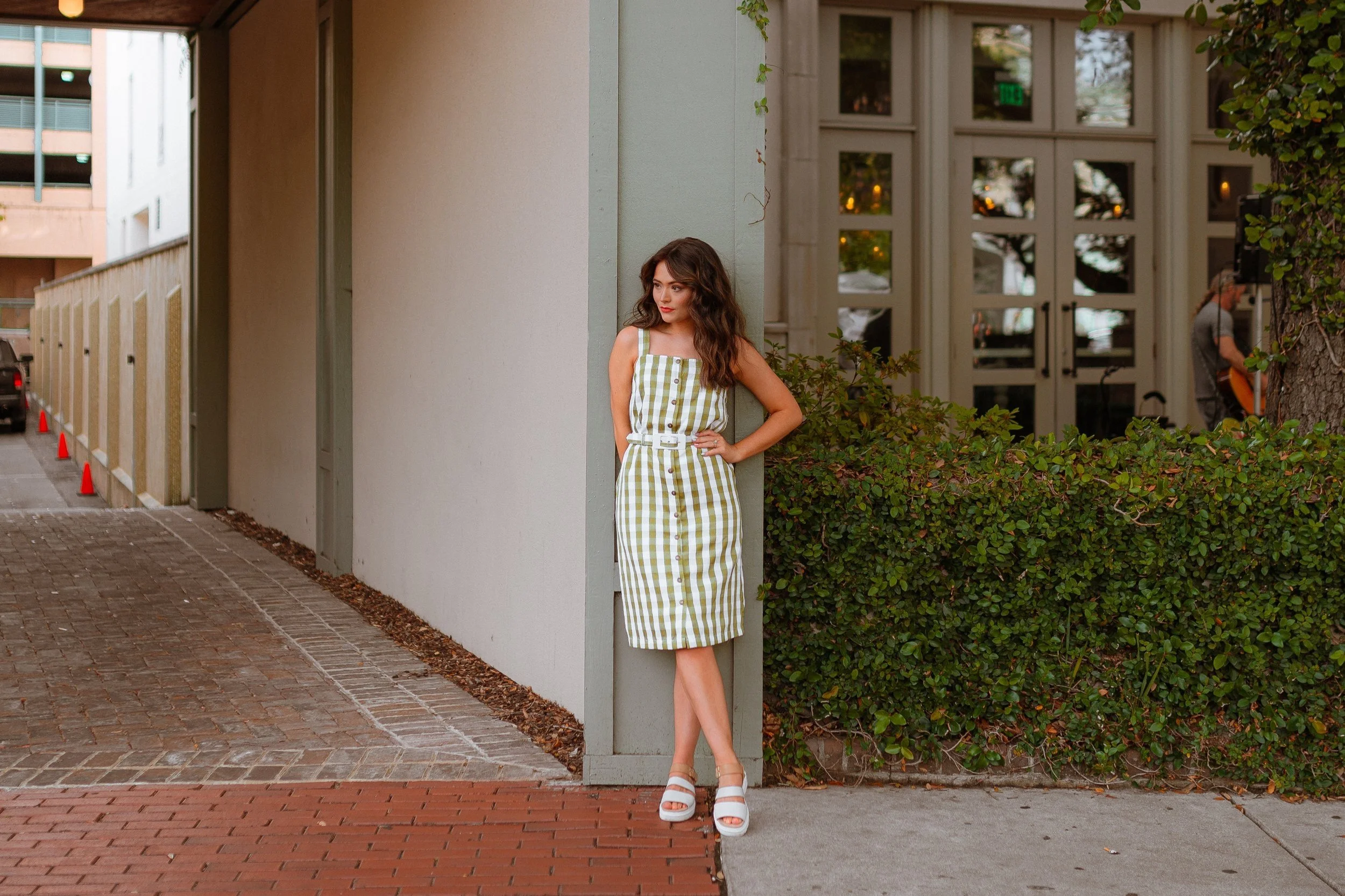 Woman in a green and white checkered dress standing next to a light-colored wall outside